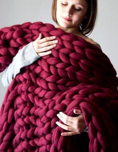 a woman wrapped in a large chunky blanket with her hands on the top of it