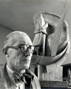 an old man wearing glasses and a bow tie in front of a wooden carving sculpture