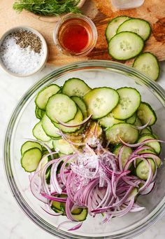 cucumber and onion salad in a glass bowl on a marble counter top with dressing