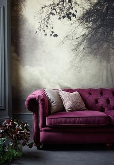 a purple couch sitting in front of a window next to a vase filled with flowers