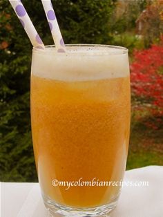 a tall glass filled with orange liquid and two straws in the top, sitting on a table outside