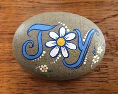 a painted rock with the word joy written in blue and white on it, sitting on a wooden surface