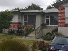 a blue car is parked in front of a house with red brick and white trim