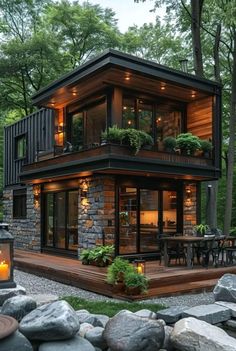 a small house with lots of windows and lights on the front, surrounded by rocks