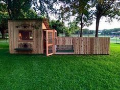 a dog house built into the side of a fenced in area with grass and trees