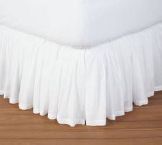 a white bed skirt with ruffles on the top and bottom, sitting on a hardwood floor