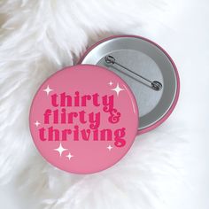 a pink button with the words thirty, flirty and thriving on it sitting next to a white furry surface