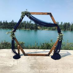 a wooden frame decorated with flowers and greenery on the edge of a body of water