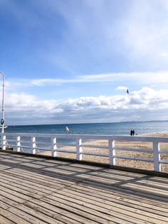 there is a bench on the boardwalk by the water and people are in the distance