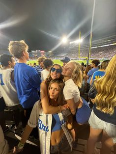 two girls hugging each other in front of a crowd at a baseball game with the lights on