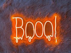 the word boo spelled out with neon lights on top of a furry surface in front of an orange light