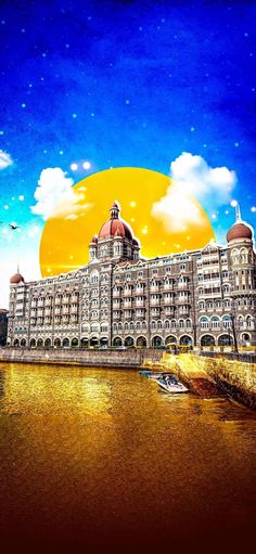 a large building sitting on the side of a river under a blue sky with clouds