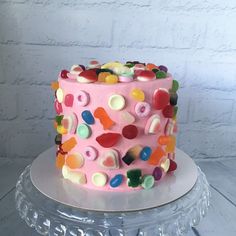 a pink cake decorated with gummy bears on top of a glass stand next to a brick wall