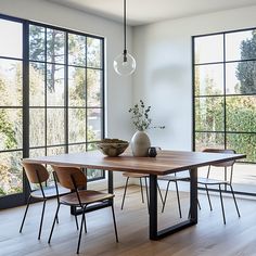 a dining room table with chairs and a vase on the table in front of large windows