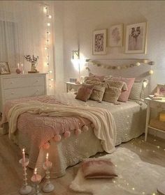 a bedroom decorated in pink and white with candles on the bed, lights strung from above