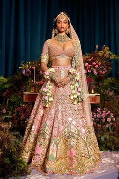 a woman in a pink and gold bridal gown standing on a stage with flowers