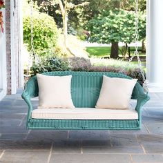 a green couch sitting on top of a stone floor next to a white porch swing