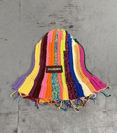 a multicolored crocheted hat hanging from a hook on a gray wall