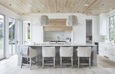 a large kitchen with white cabinets and gray counter tops, along with four chairs at the center island