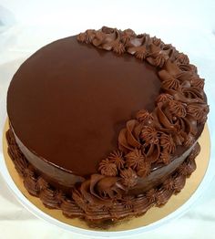 a chocolate cake on a white plate with brown icing and flowers around the edges