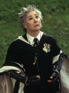 an older woman with grey hair wearing a black and white outfit standing in the grass