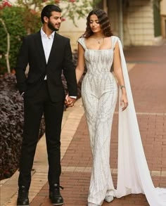 a man and woman dressed in formal wear walking down a sidewalk holding hands with each other