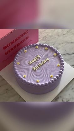 a purple birthday cake sitting on top of a table next to a card and box