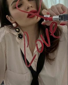 a woman with red lipstick holding the word love in front of her face while wearing a white shirt and black tie