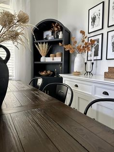 a wooden table topped with a black vase filled with dried flowers next to a book shelf