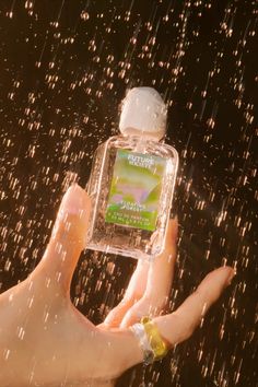 a person's hand holding up a bottle of water in the air with rain coming down on them