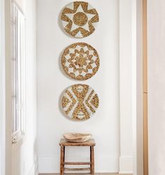 three decorative plates mounted on the wall above a stool in a white room with an open door