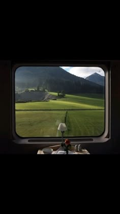 a view from the inside of a train window looking out onto a green field with mountains in the distance