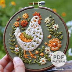 a person holding up a small embroideryed chicken in front of some daisies and flowers