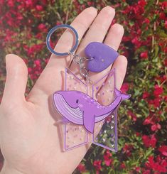 a hand holding a purple whale keychain and a plastic bottle opener in it's palm