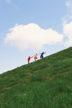 three people standing on top of a green hill with their arms in the air while holding hands