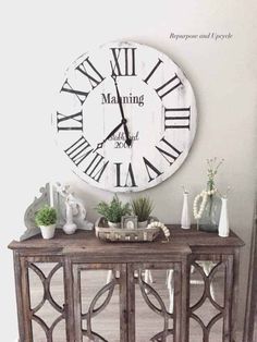 a large clock mounted to the side of a wall next to a table with vases on it