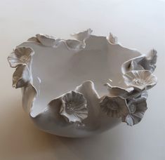 a white bowl with flowers on it sitting on a table next to a wall or floor