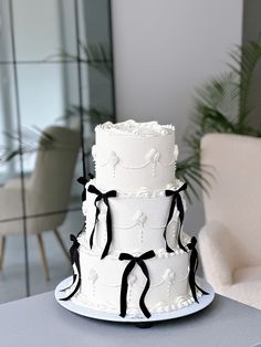 a three tiered white cake with black ribbons on it sitting on top of a table