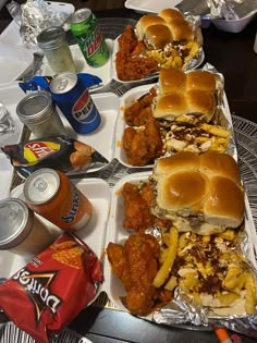 several trays filled with sandwiches and condiments next to cans of soda on a table