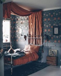 a bed sitting in a bedroom next to a window with red drapes on it