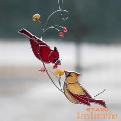 a stained glass bird decoration hanging from a branch with berries on it's tail