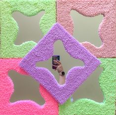 a person taking a selfie in front of a mirror with pink, green and purple squares on it