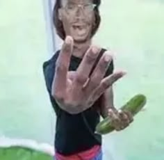 a woman making the vulcan sign with her hand and holding a cucumber in front of her face