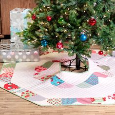 a small christmas tree with presents under it on the floor next to a tablecloth