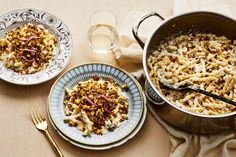 two plates with food on them next to a pot of pasta and a glass of water