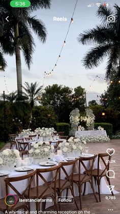 a table set up with white flowers and greenery for an outdoor wedding reception in the evening