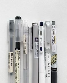 several pens and markers lined up on a white surface with one pen in the middle