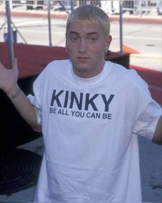 a man in a white shirt is holding his hand up to the side while standing outside