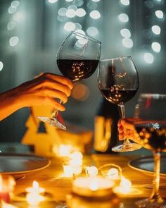 two people toasting wine glasses at a dinner table with lit candles in the background