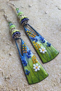 two green and blue earrings with flowers hanging from it's sides on the sand